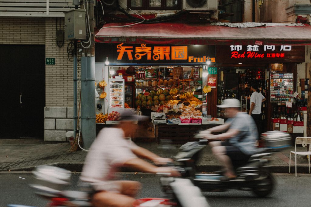 Dynamic image of motorcyclists passing a vibrant fruit stand on Shanghai street.